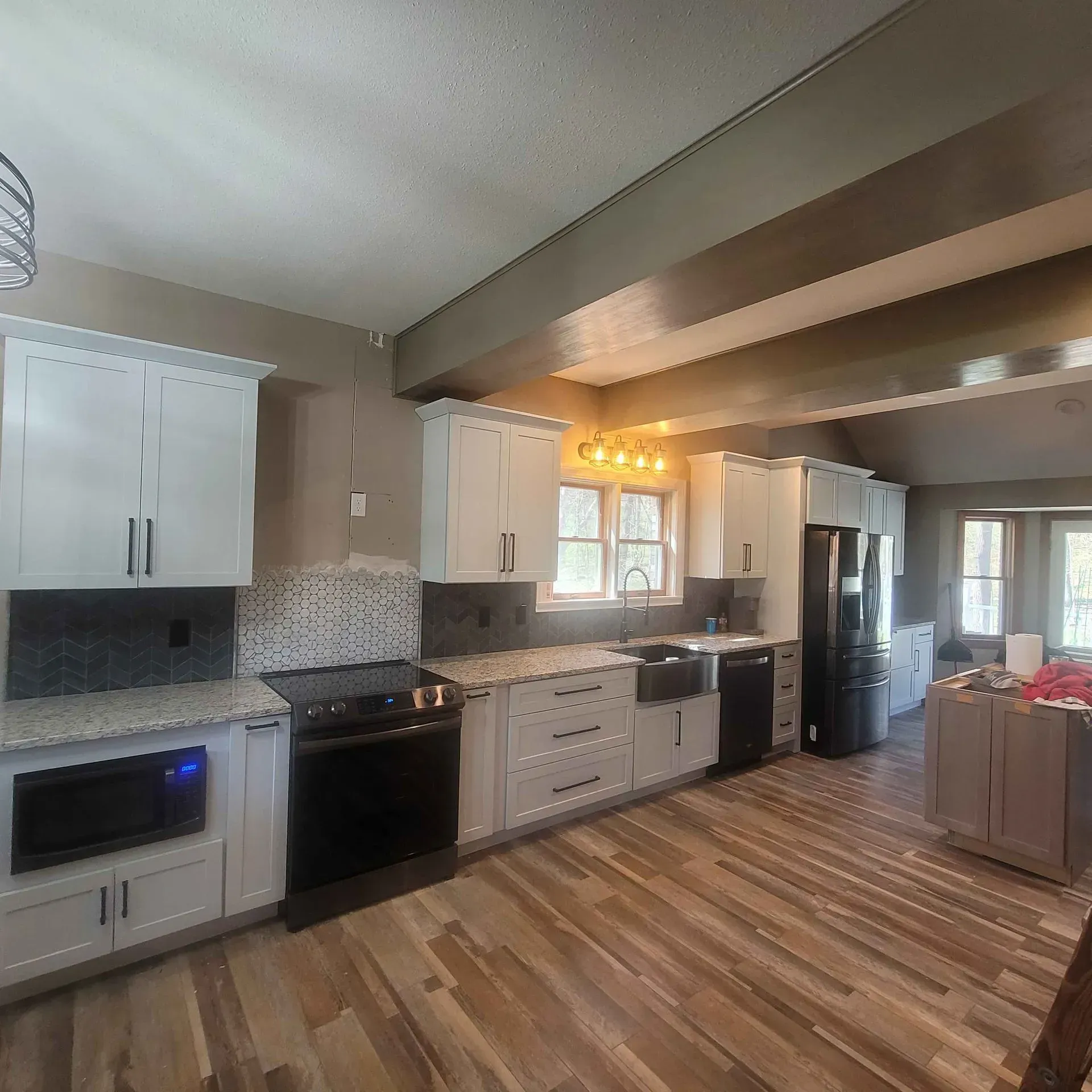 A kitchen with white cabinets , black appliances , and a wooden floor.