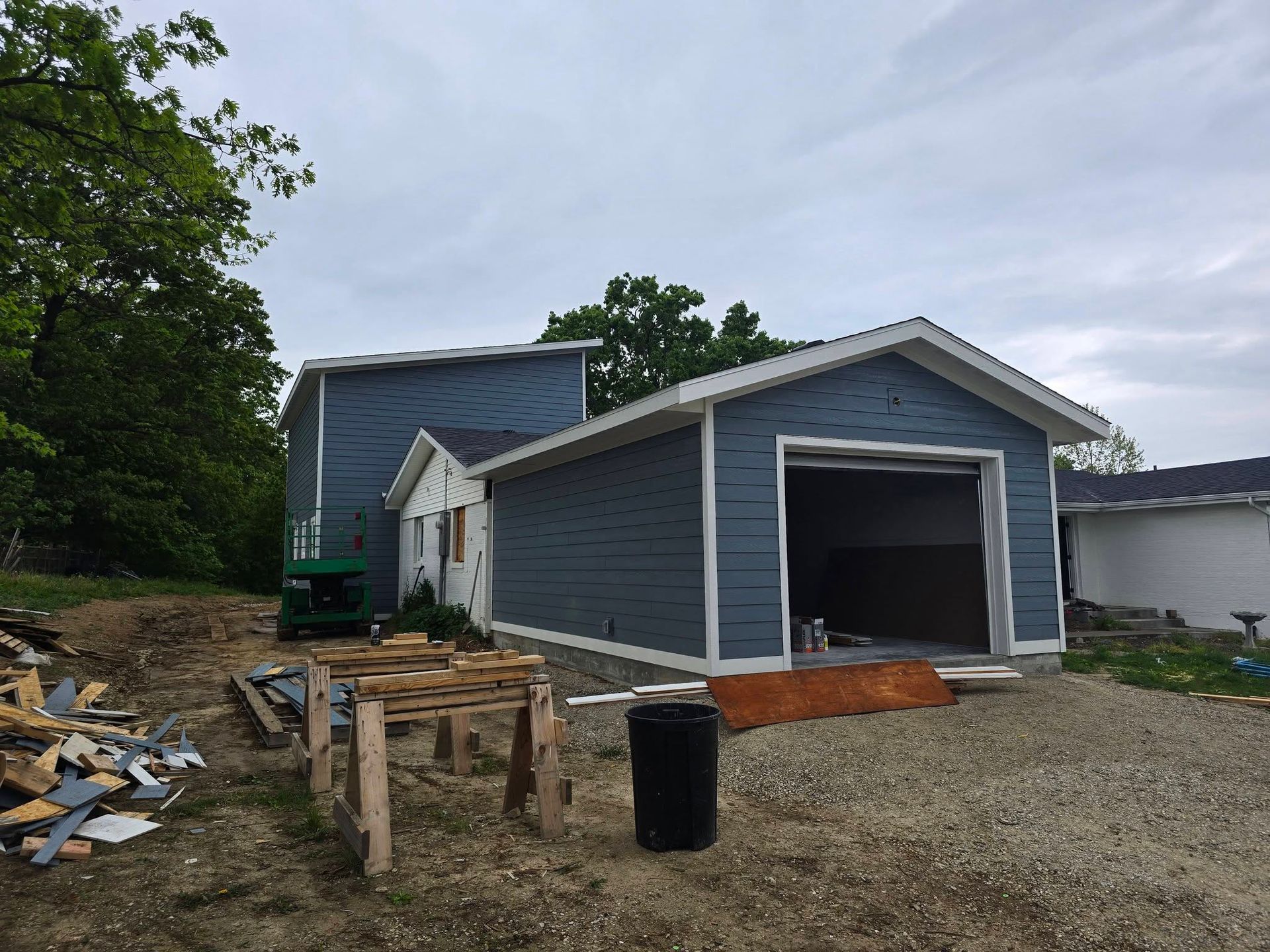 Blue siding is being installed on a house and attached garage under construction, with a pile of scrap materials nearby.