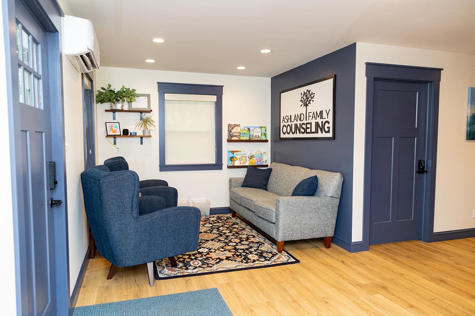 Waiting room with blue and gray furniture, rug, and walls, with door and window.