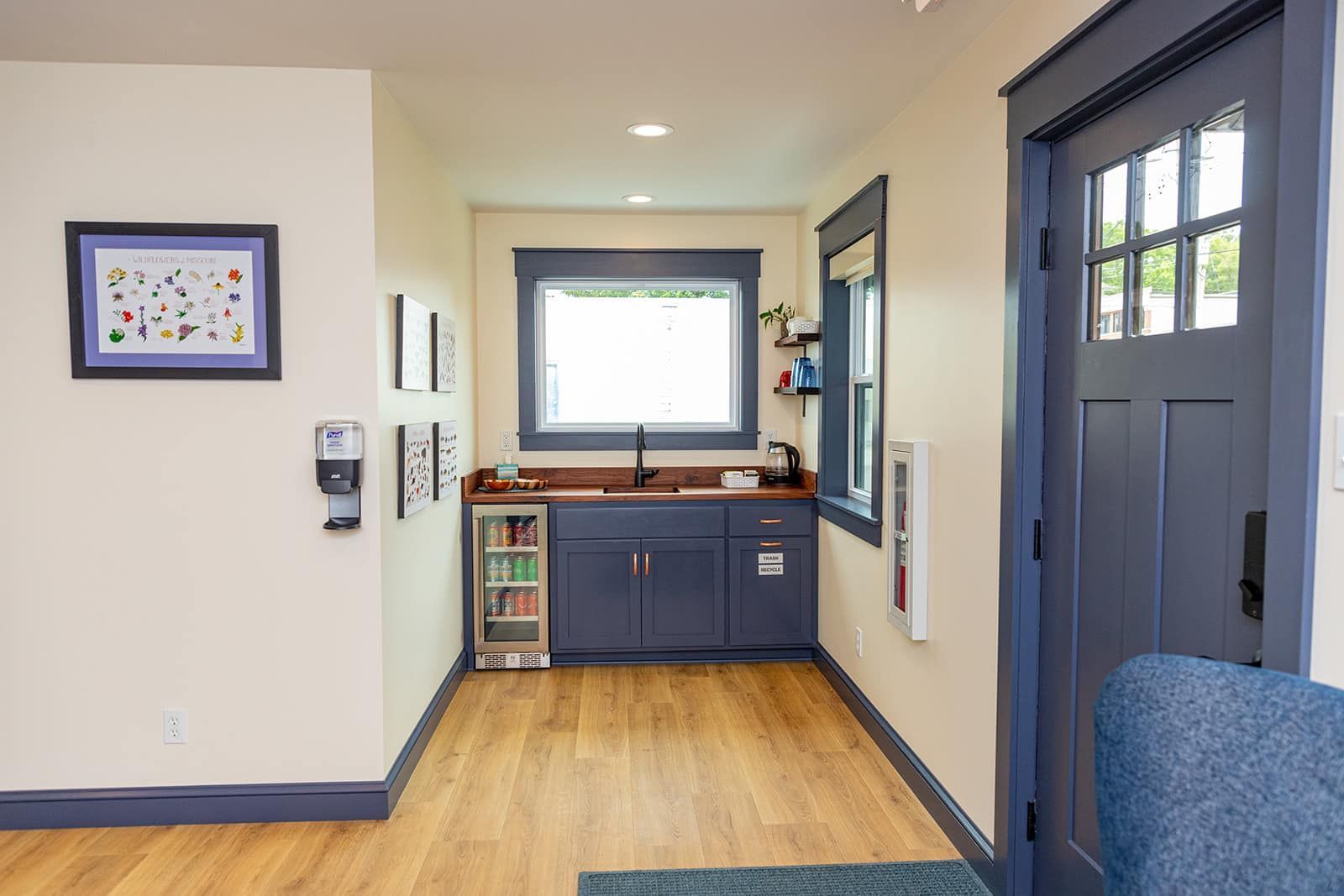 Bright hallway with blue trim, wooden floor, cabinets, and a window at the far end.