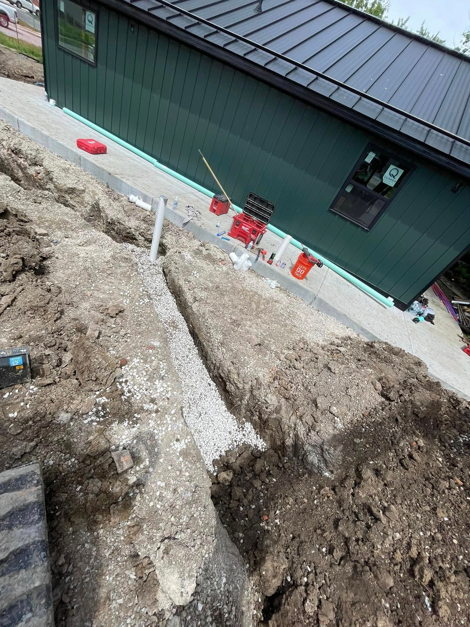 Gravel landscaping beside a green house, with a white walkway and orange cones along the foundation.