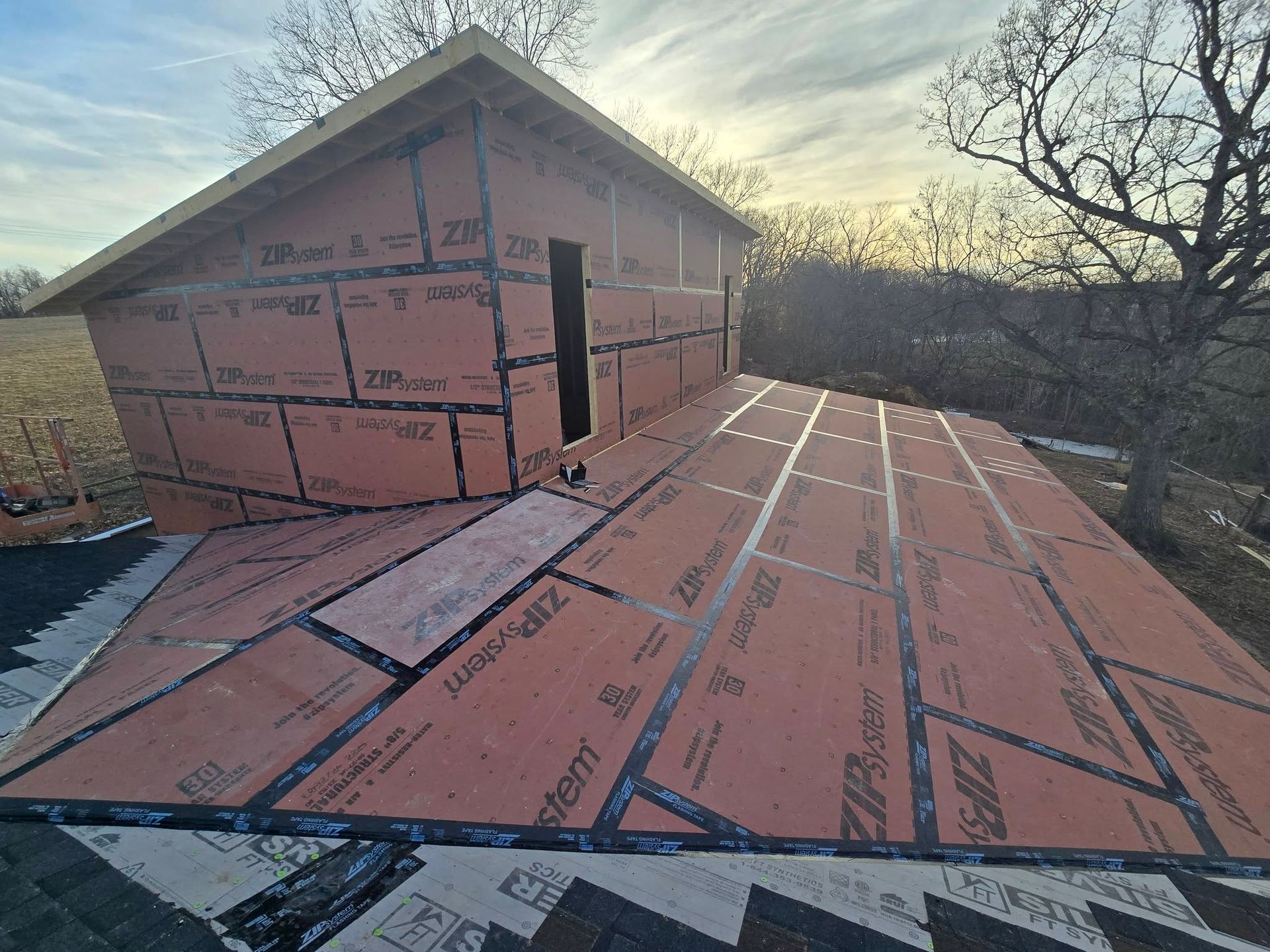Building under construction with red siding and exposed roof decking, outdoors.