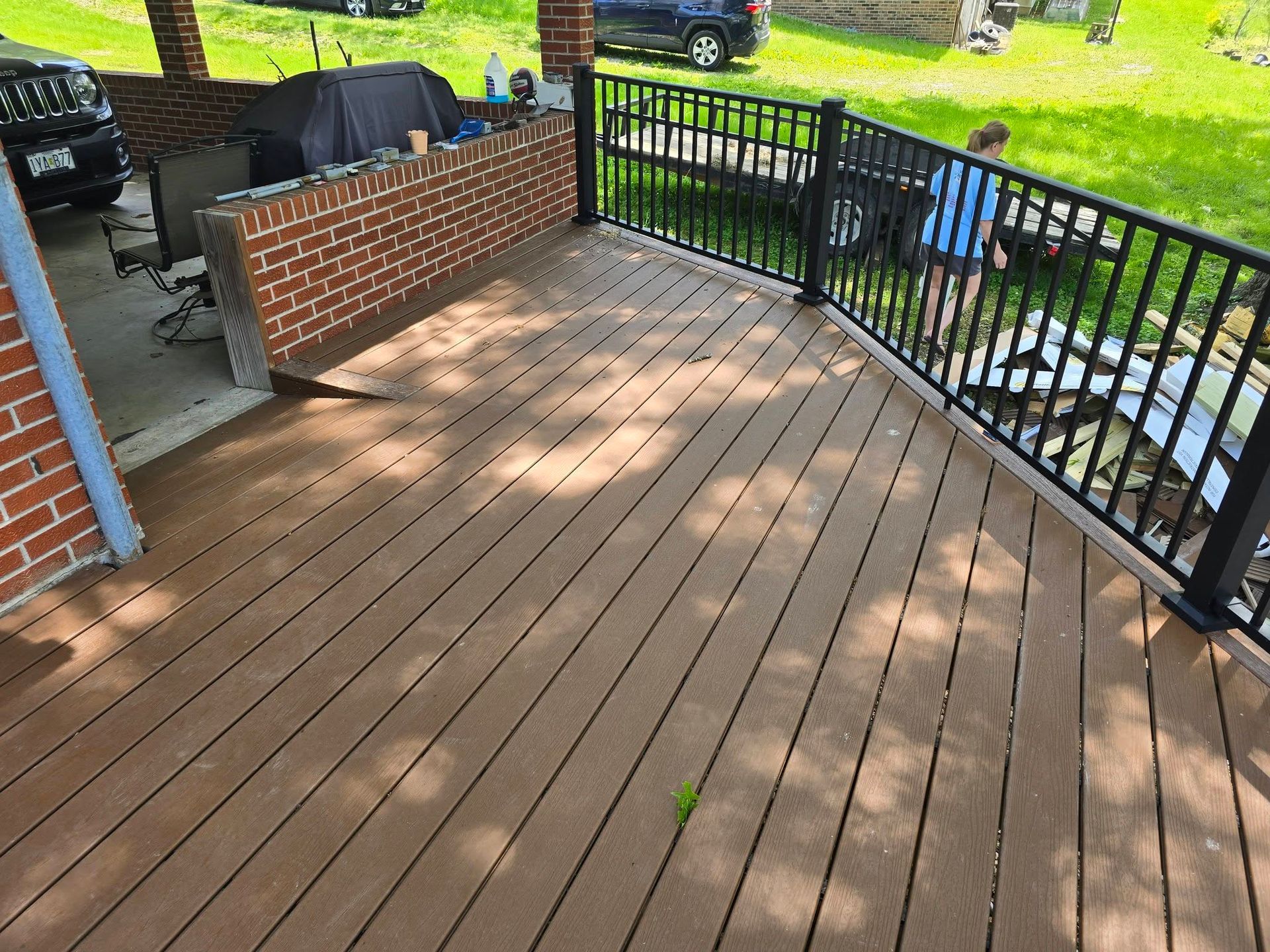 Brown deck with black railing and brick wall. A person stands near the railing.