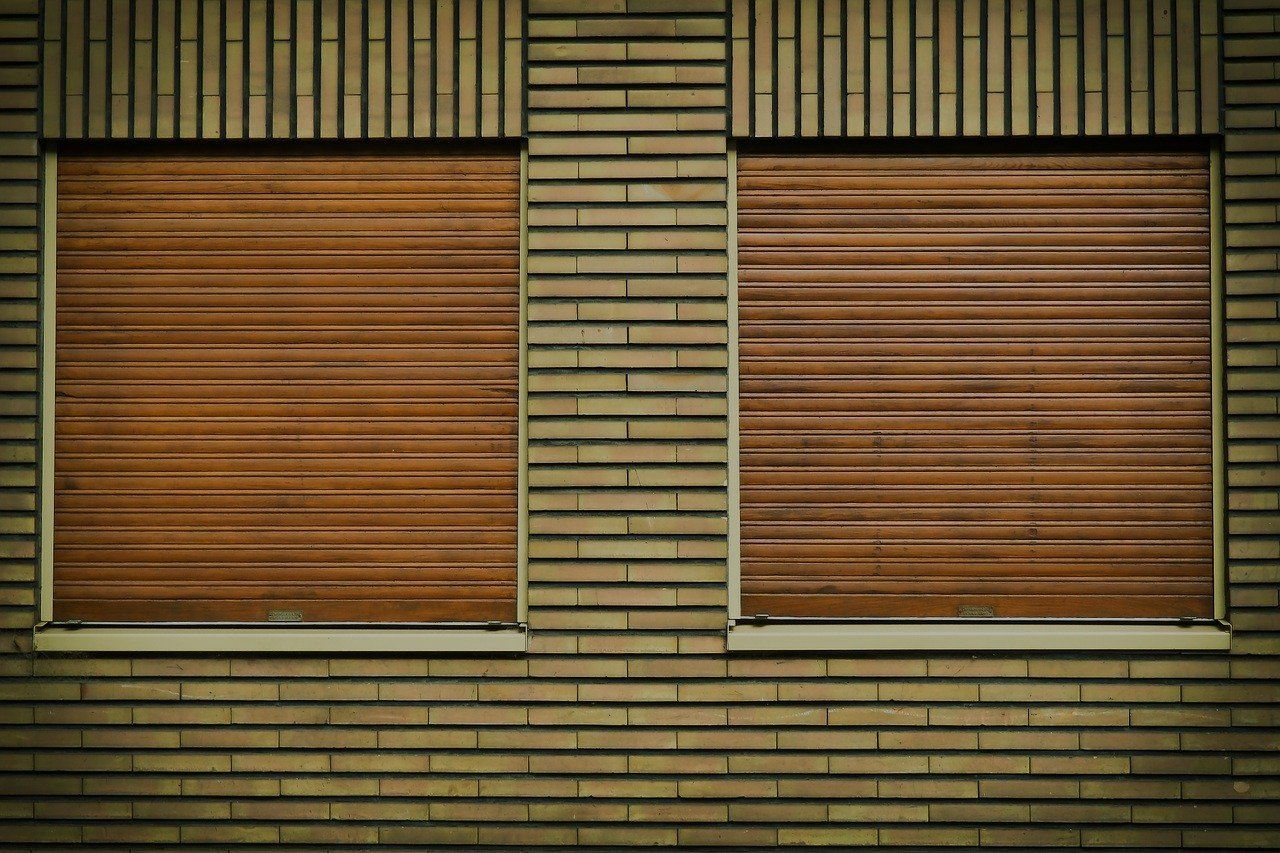 Due finestre con persiane marroni orizzontali chiuse su un edificio in mattoni.