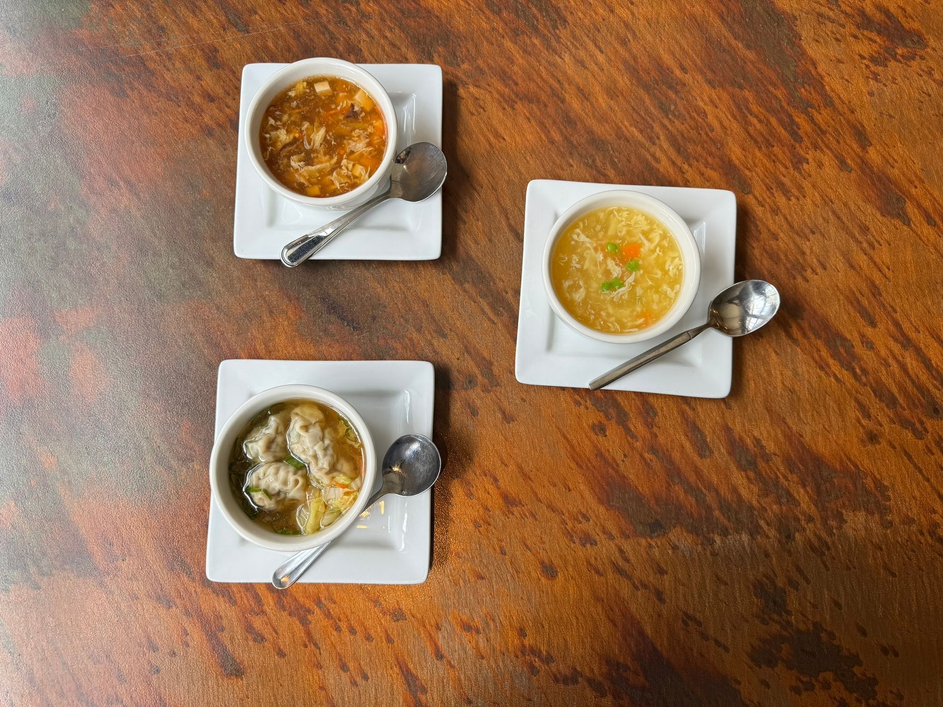 Three bowls of soup with spoons on a wooden table.