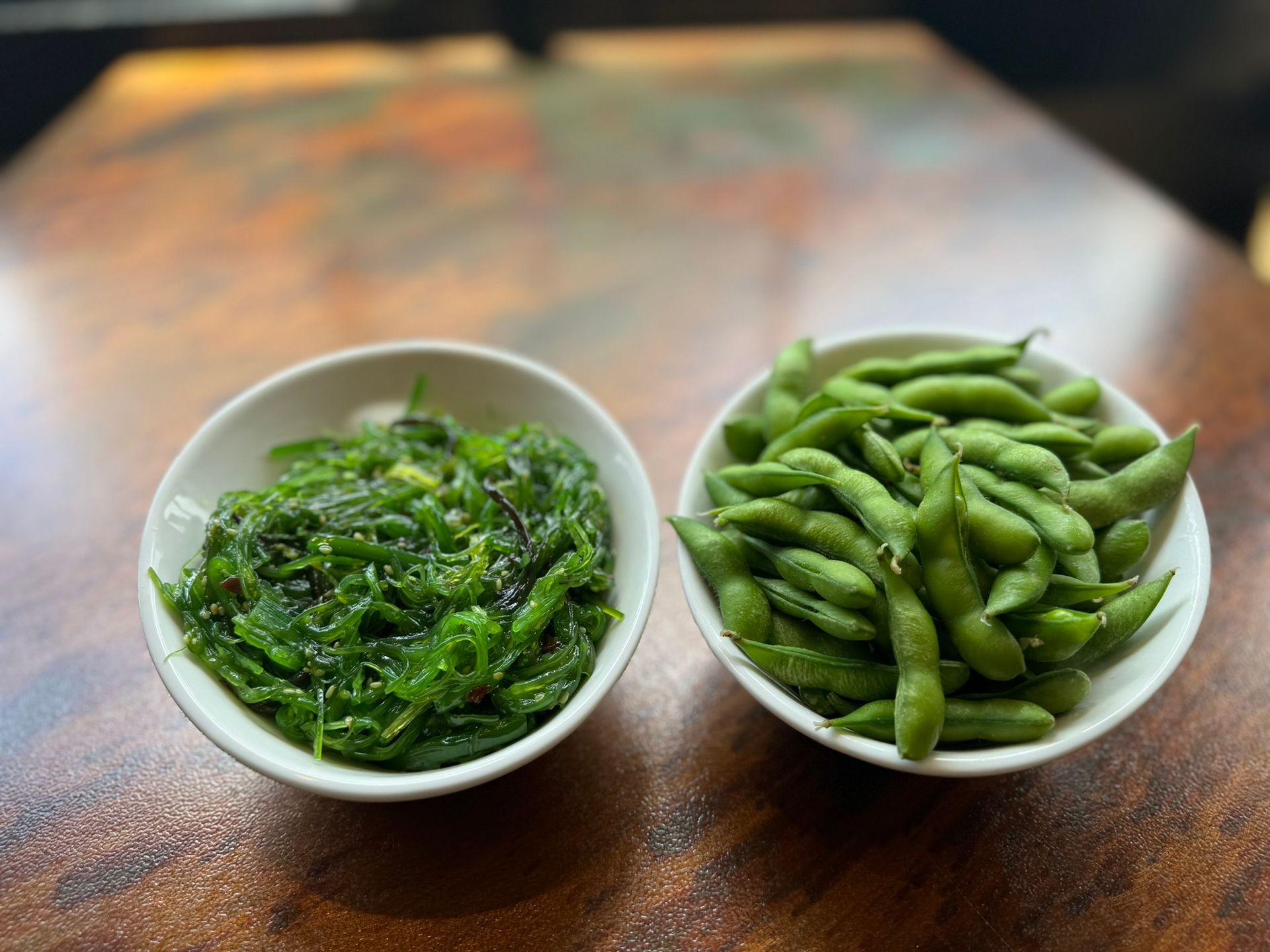 Two bowls of green vegetables are sitting on a wooden table.