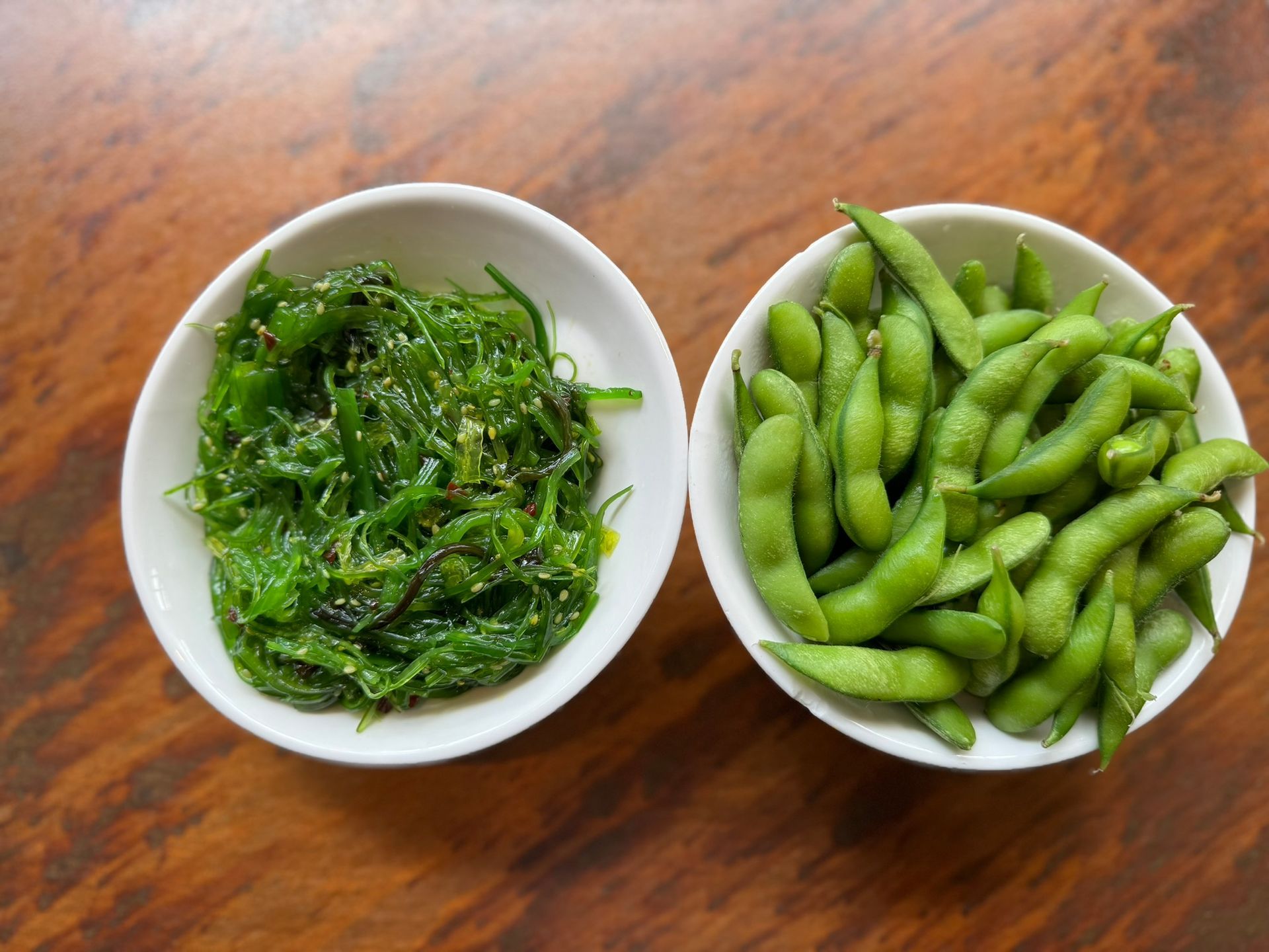 Two bowls of seaweed and edamame on a wooden table.