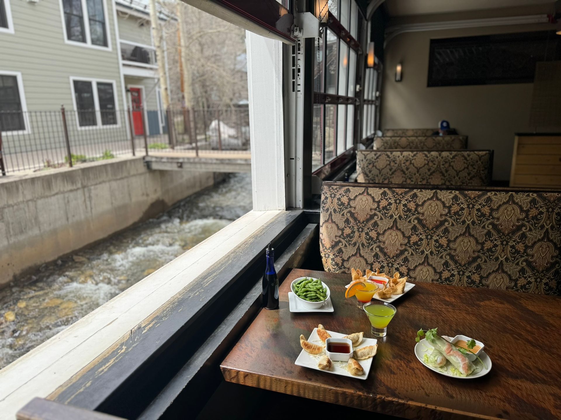 A table with plates of food and a martini on it in front of a window overlooking a river.