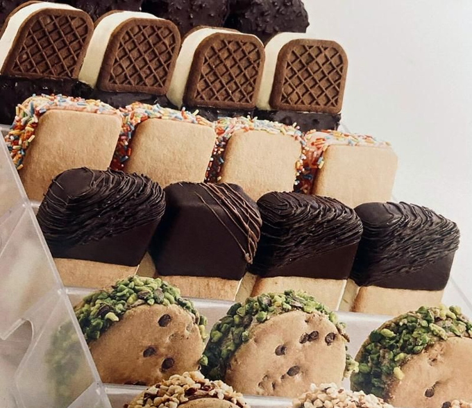 Barrette e biscotti assortiti decorati, disposti in file su un vassoio da esposizione.