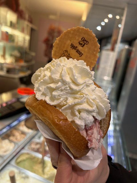 Un sandwich di gelato con panna montata e un biscotto in mano in una gelateria.
