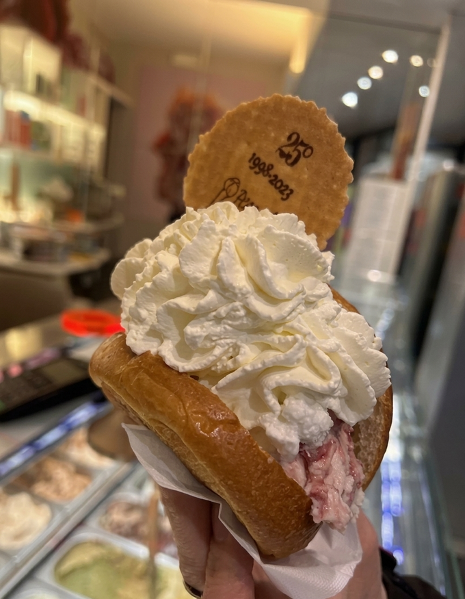 Sandwich di gelato monoporzione guarnito con panna montata, esposto in un'area di vendita.