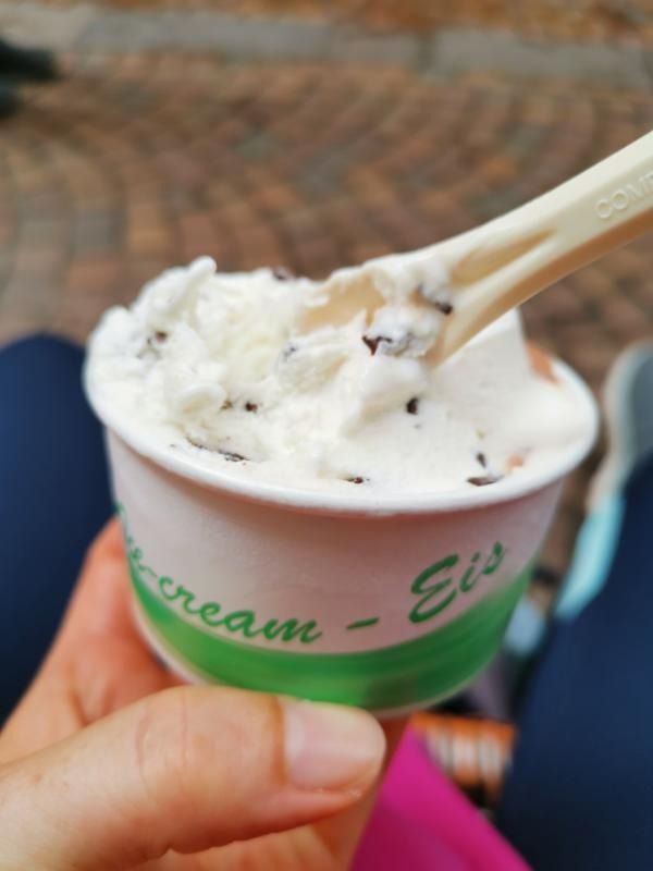 Una mano che tiene una tazza di gelato bianco con un cucchiaio che ne preleva una porzione.