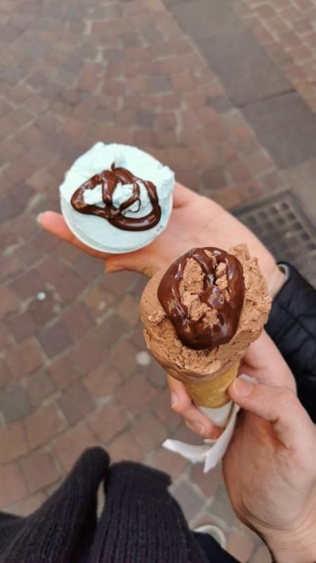 Due coni gelato, uno bianco con glassa al cioccolato e uno al cioccolato, tenuti all'aperto su un marciapiede di mattoni.