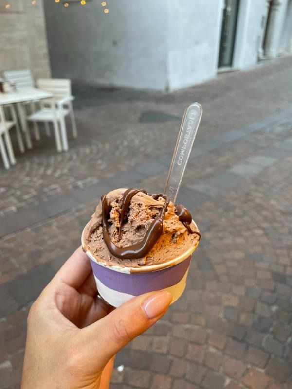 Una mano che tiene una piccola tazza di gelato al cioccolato con un cucchiaino in un caffè all'aperto.