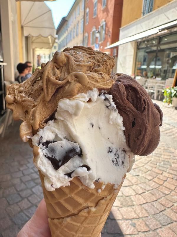 Cono gelato con palline di cioccolato, vaniglia e caramello sulla terrazza di un caffè in una strada acciottolata.