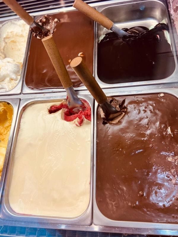 Espositore per gelati con quattro vaschette di gelato al cioccolato, vaniglia e giallo, complete di palette e cucchiaini.