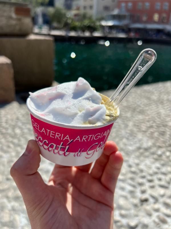 Una mano che regge una piccola coppetta di gelato con un cucchiaino in riva al mare.
