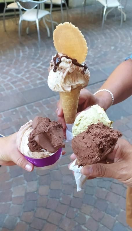 Quattro mani che reggono diversi coni gelato in un bar.