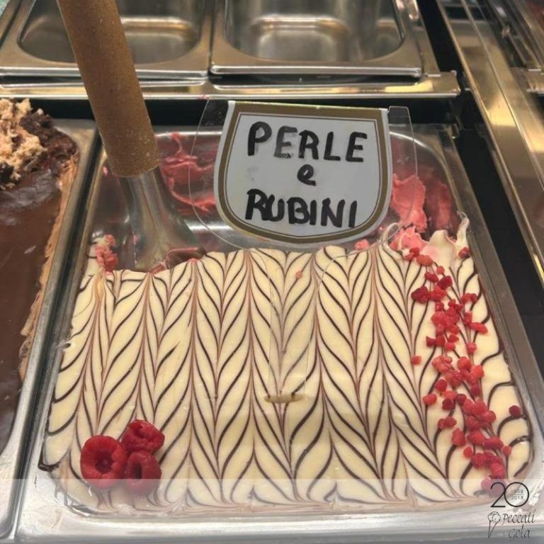 Esposizione di gelato con dessert alla crema a strisce etichettato “Perle e Rubini”, guarnito con frutti rossi e pezzi di ciliegia.