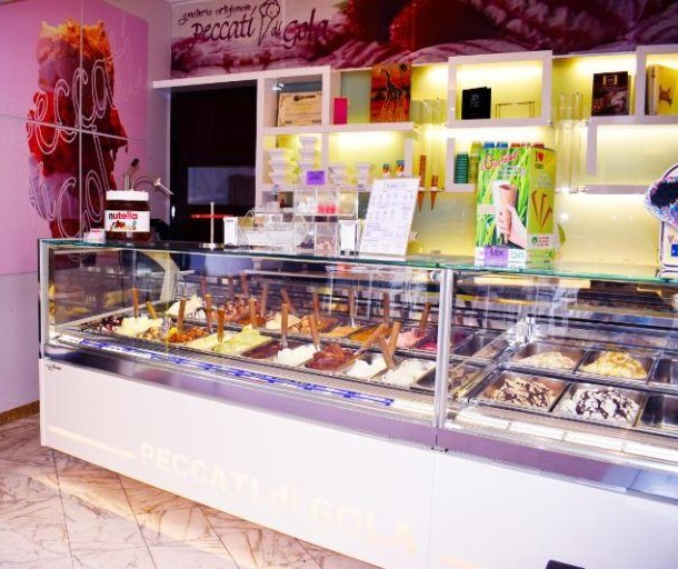 Bancone di una gelateria rosa acceso con vetrine e scaffali pieni di dessert colorati alle sue spalle.