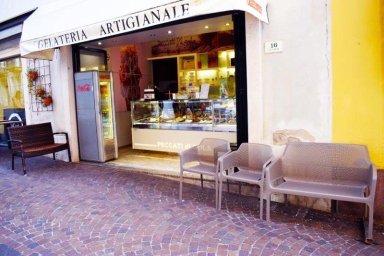 Vetrina artigianale con bancone espositivo, porta d'ingresso aperta e tavolini all'aperto su una strada acciottolata