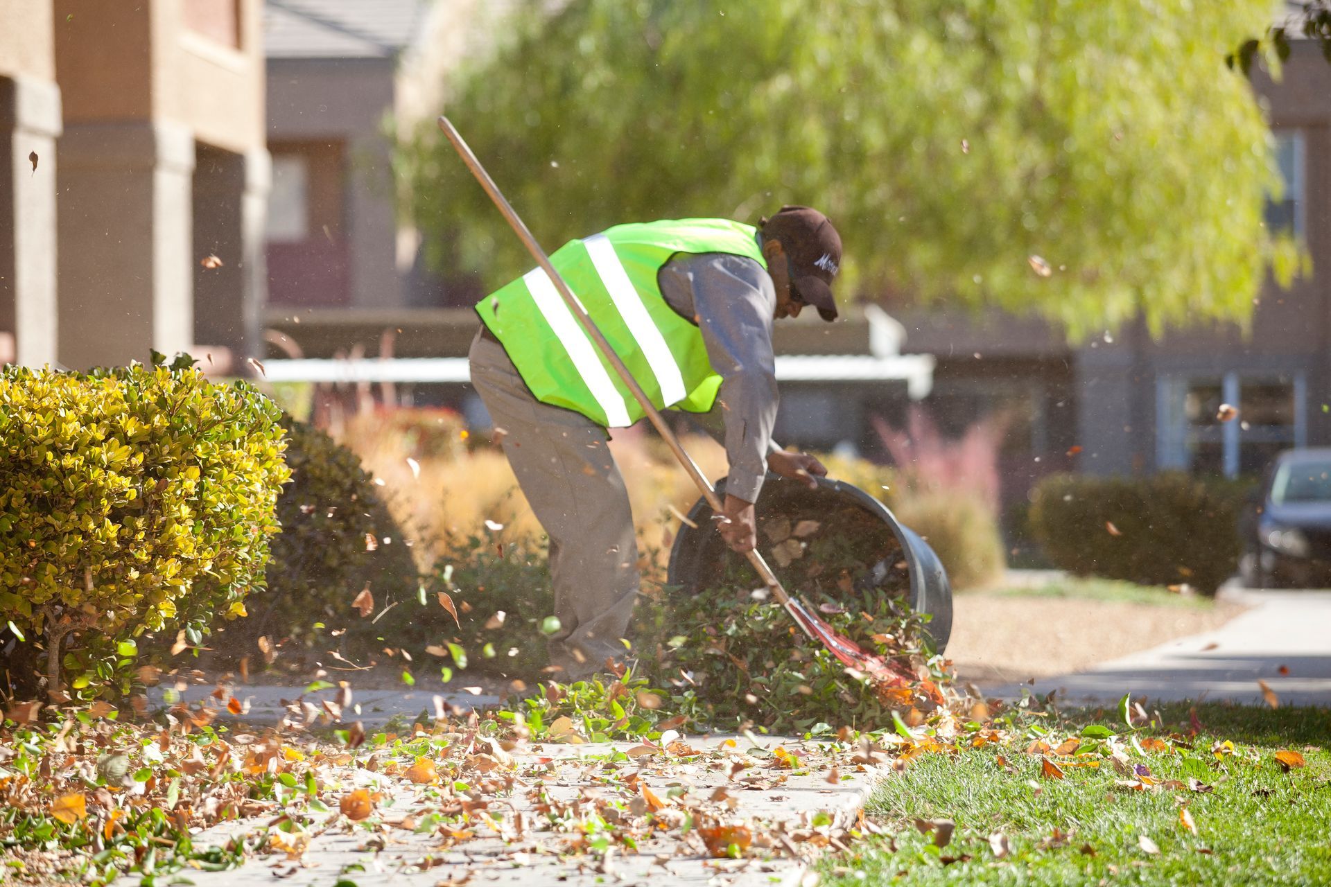 A man in a green vest is raking leaves in a yard.