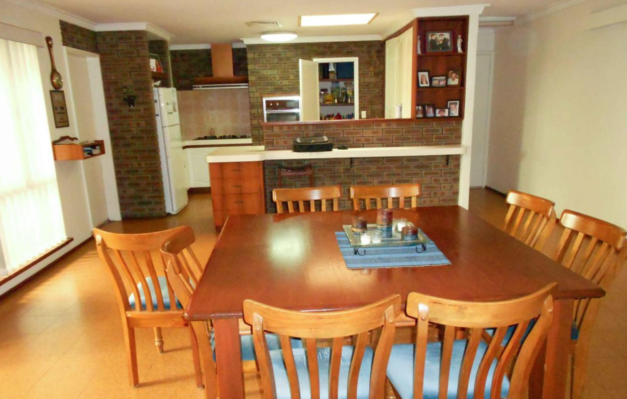 A dining room with a table and chairs and a kitchen in the background