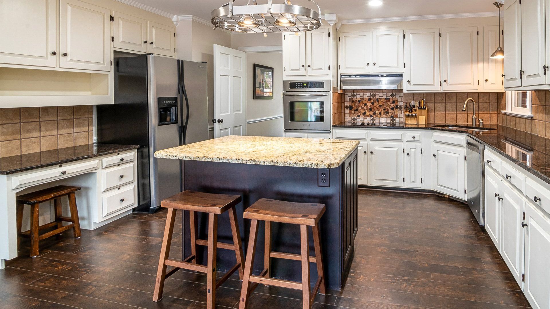 A large kitchen with white cabinets , stools , a refrigerator and a large island.
