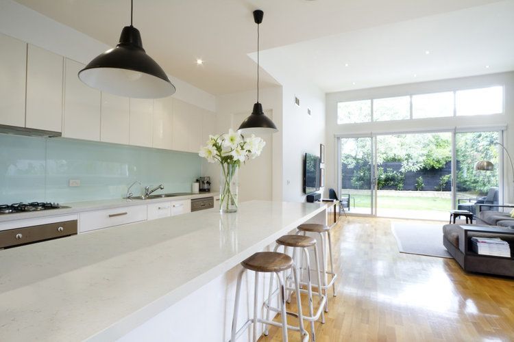 A kitchen with white cabinets and stools and a vase of flowers on the counter.