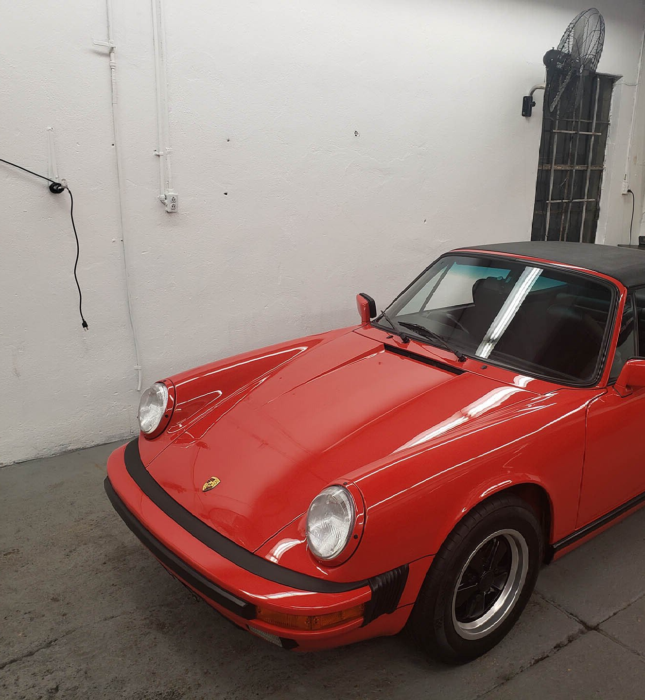 Red Porsche 911 convertible parked in a garage with a black roof and black wheels.