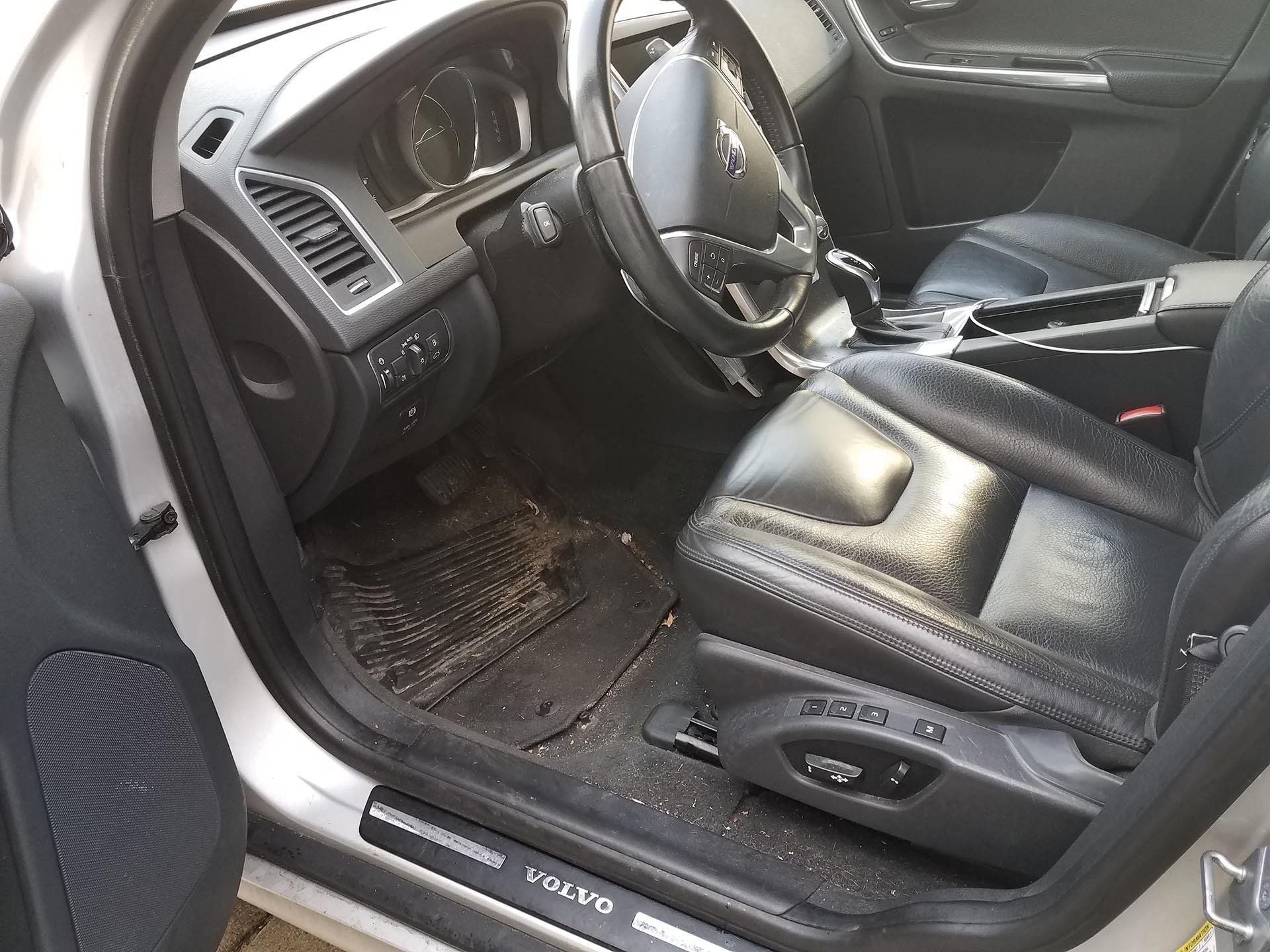 Interior of a Volvo car with dirty floor mats and black leather seats.