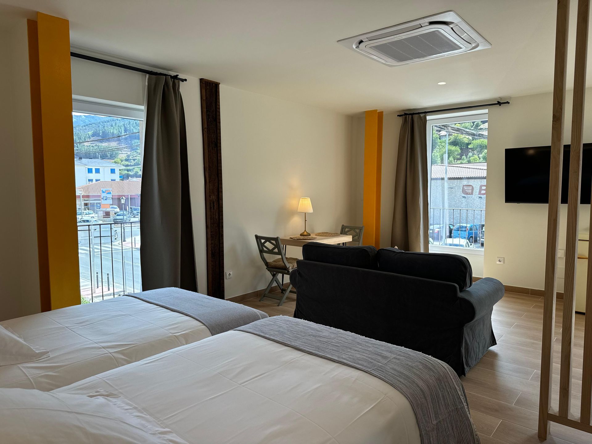 Dormitorio con dos camas individuales, sofá, mesa pequeña, dos ventanas y TV.