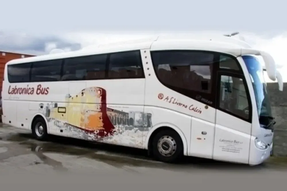 Un autobus bianco della Labronica parcheggiato all'aperto con una grafica dipinta raffigurante un edificio e il logo dell'AS Livorno Calcio sul fianco.