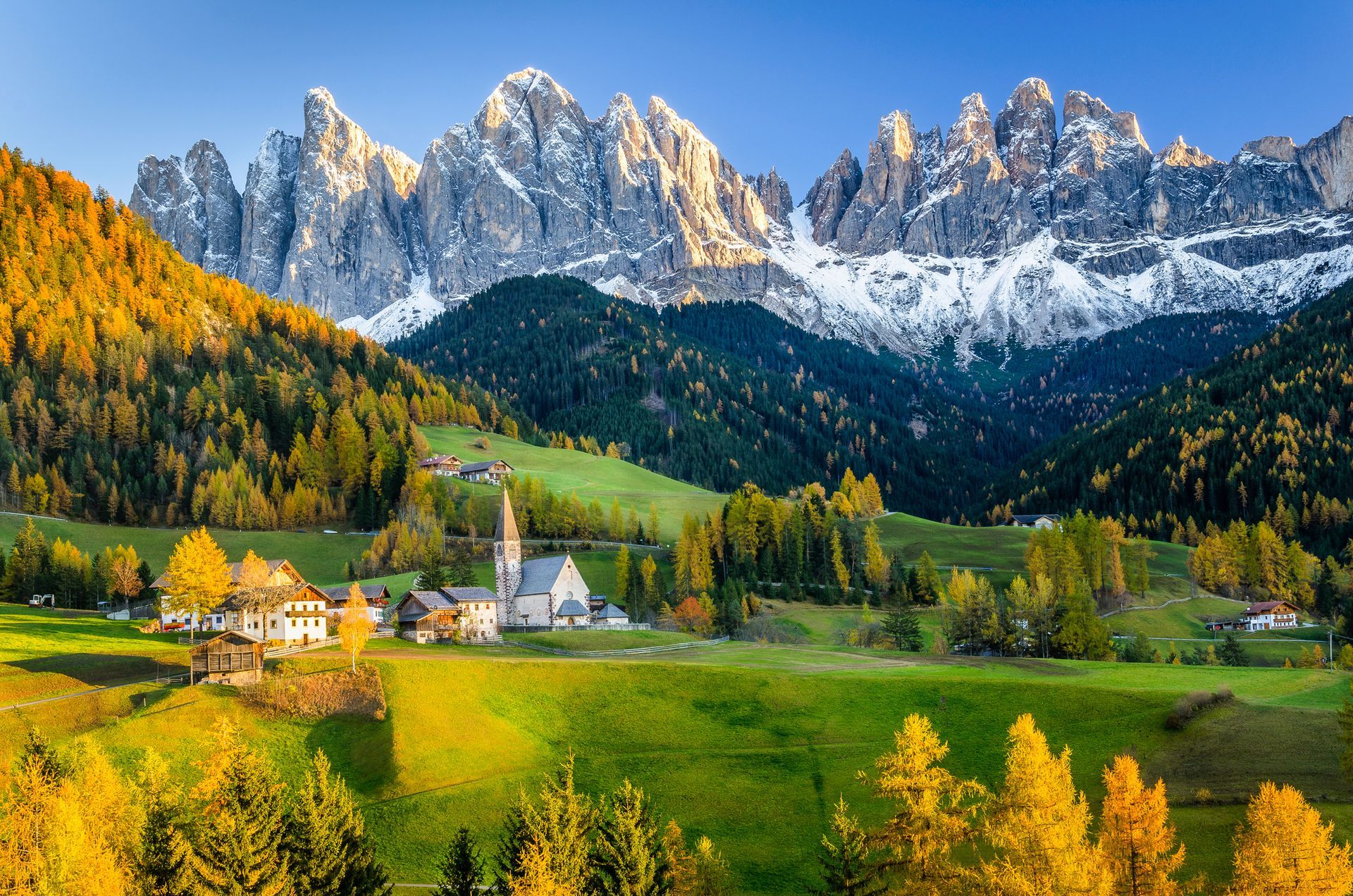 Un incantevole villaggio alpino con una piccola chiesa incastonata in una verde vallata, ai piedi delle aspre cime innevate delle Dolomiti.