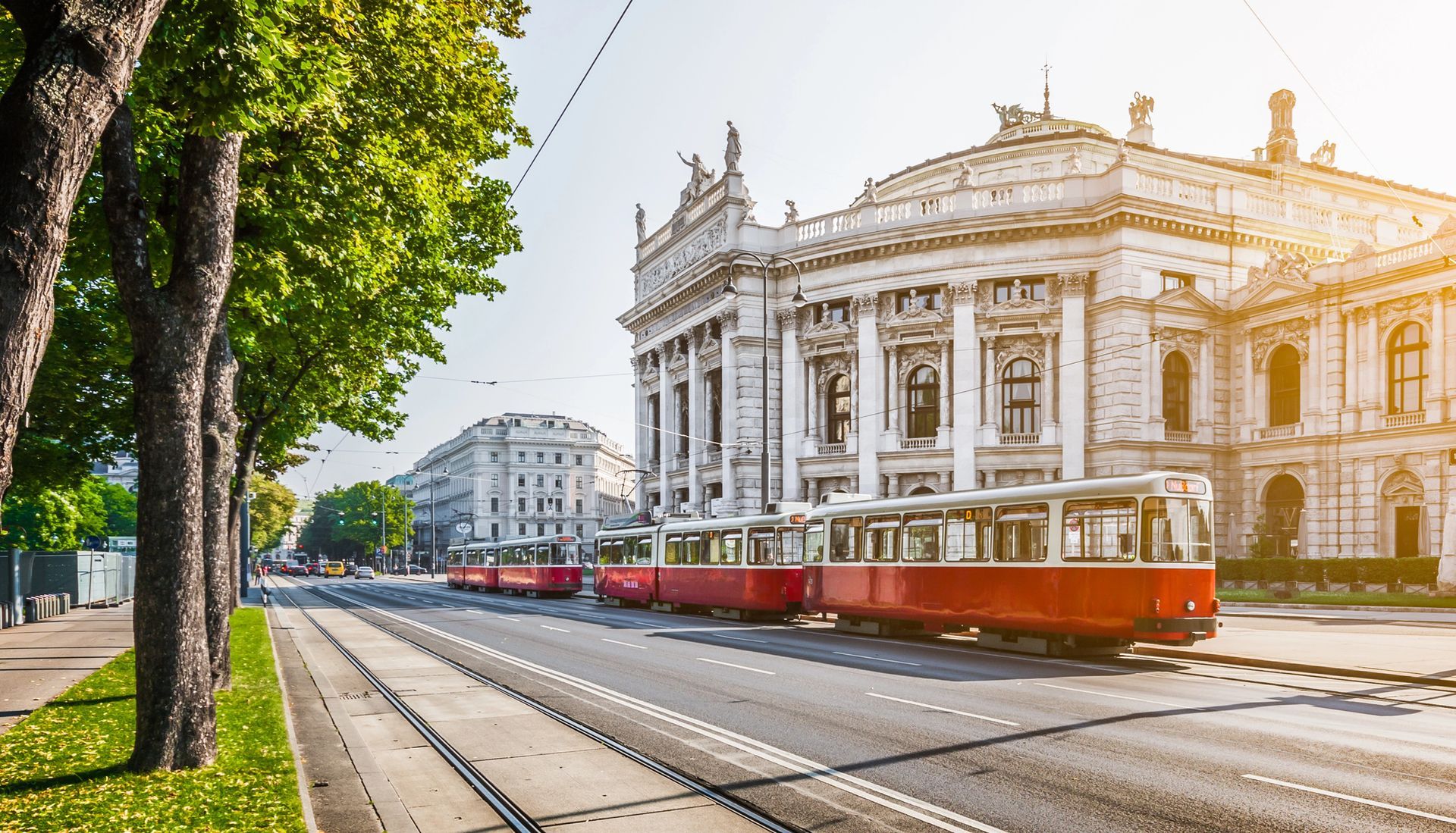 Un tram rosso passa davanti all'elegante edificio del Burgtheater in una strada soleggiata di Vienna, in Austria.