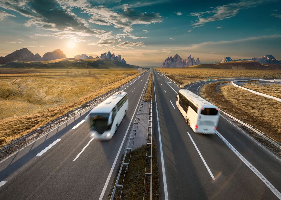 Vista dal retro di un autobus con passeggeri seduti su sedili blu, che guardano verso il parabrezza luminoso e illuminato dal sole.