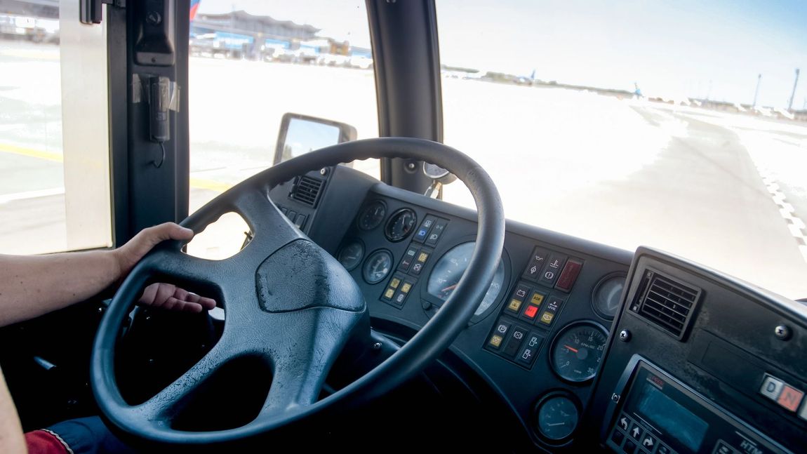 Vista dalla prospettiva del conducente dall'abitacolo di un veicolo sulla pista di un aeroporto, con il volante in primo piano.