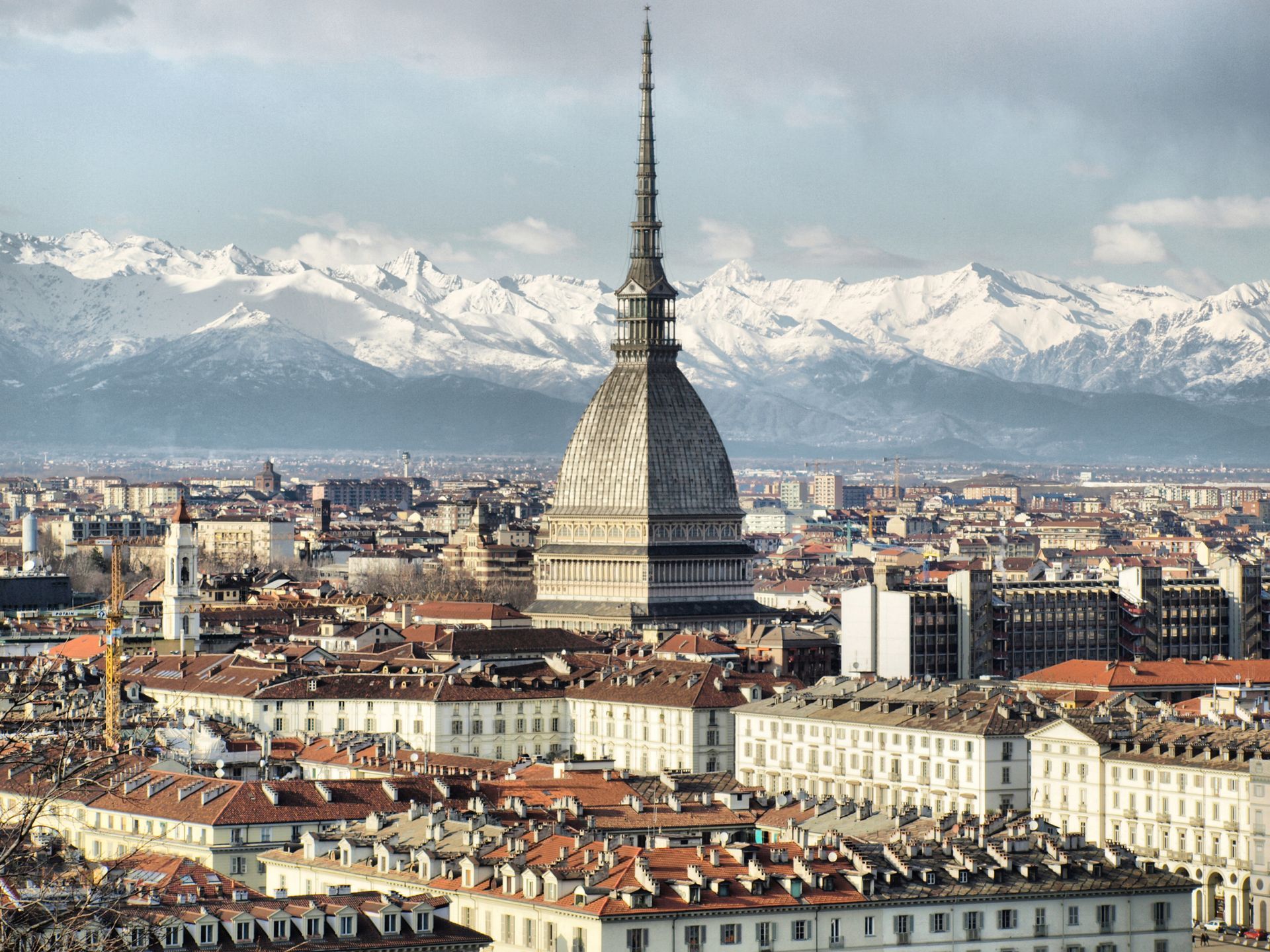 La torre della Mole Antonelliana si erge sullo skyline di Torino, incorniciata da montagne innevate sotto un cielo luminoso.