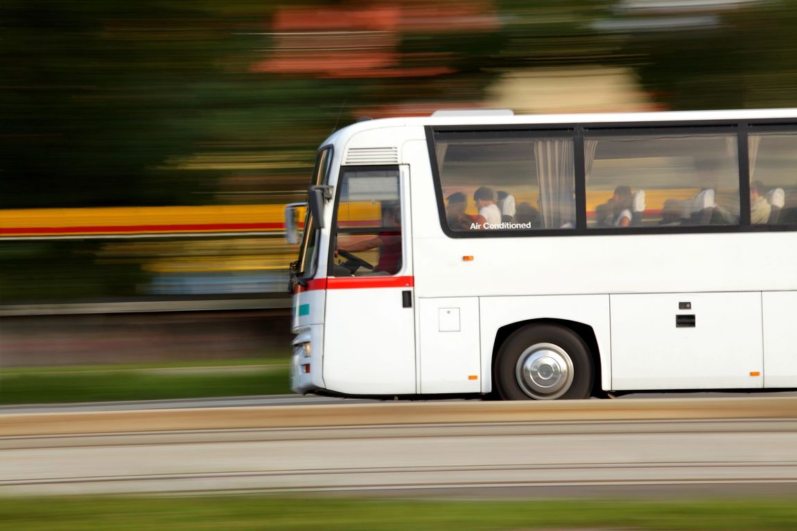 Un autobus bianco si muove velocemente lungo una strada, lo sfondo sfocato suggerisce l'alta velocità.