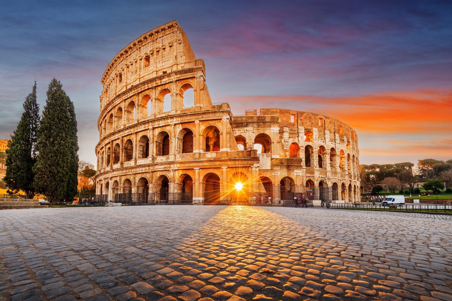 Il Colosseo di Roma illuminato dalla luce dorata del tramonto, visto da una piazza lastricata.