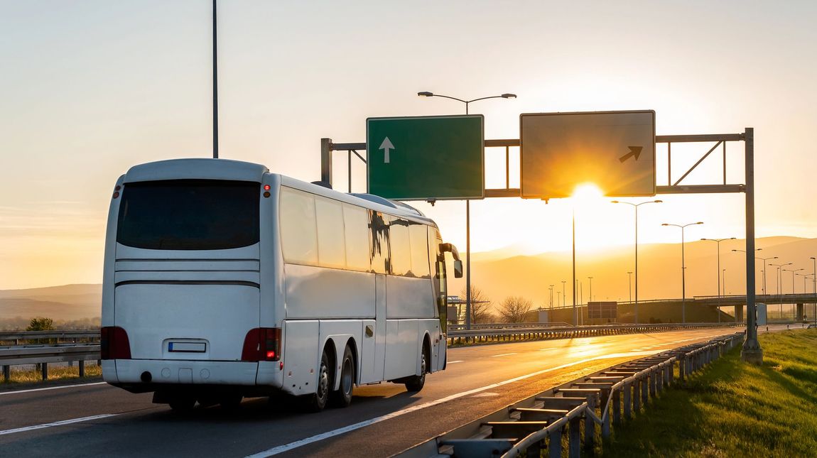 La mano di un autista è appoggiata sulla leva del cambio di un autobus, con i comandi del cruscotto visibili sullo sfondo.