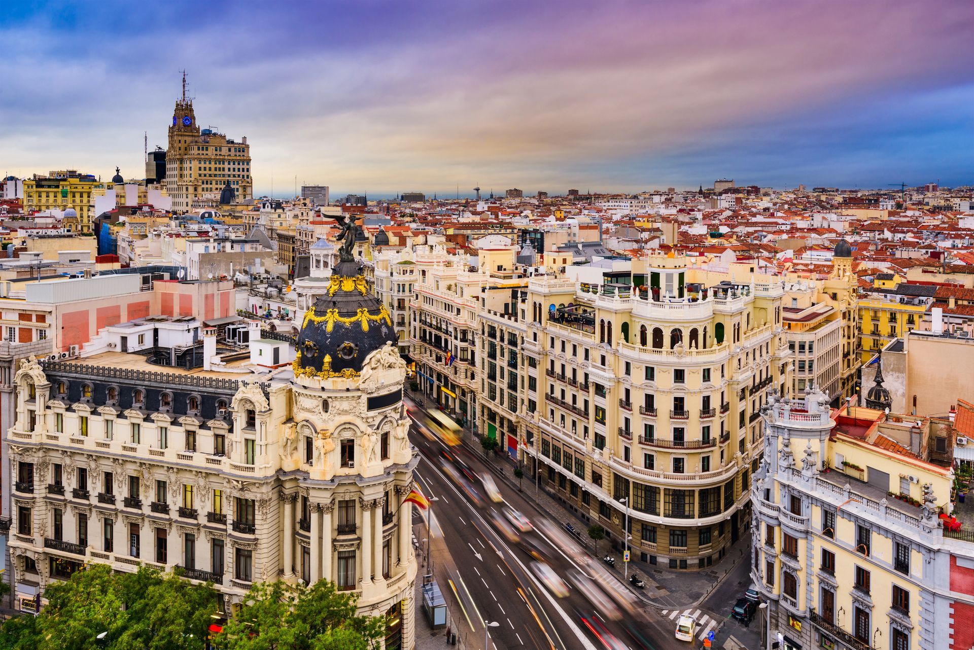 Una vista dall'alto della Gran Vía di Madrid, con i suoi edifici in pietra riccamente decorati, il Palazzo Metropolis e il traffico serale sfocato.