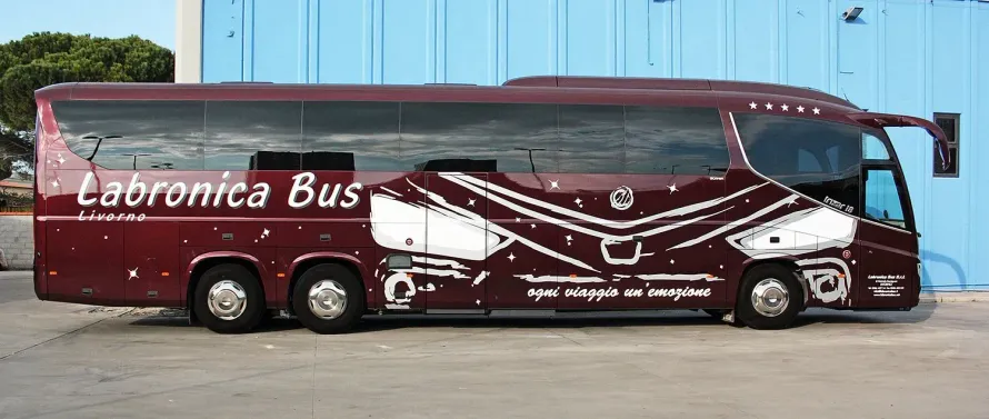 Un autobus Labronica di colore rosso scuro parcheggiato di fronte a un edificio azzurro, con disegni grafici astratti bianchi sulla fiancata.