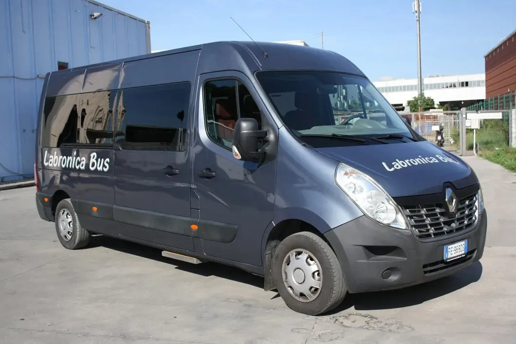 Un furgone passeggeri Renault di colore grigio scuro, parcheggiato su un piazzale asfaltato, con la scritta "Labronica Bus" sulla fiancata e sul cofano.