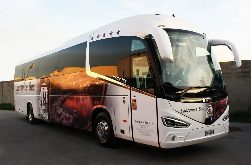 Un lussuoso autobus turistico bianco parcheggiato all'aperto, con una grande grafica raffigurante un tramonto sul fianco e il logo aziendale vicino alla parte anteriore.