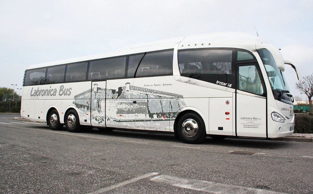 Un autobus bianco della compagnia Lebrona Bus parcheggiato su un piazzale asfaltato con una grafica decorativa grigia lungo la fiancata.