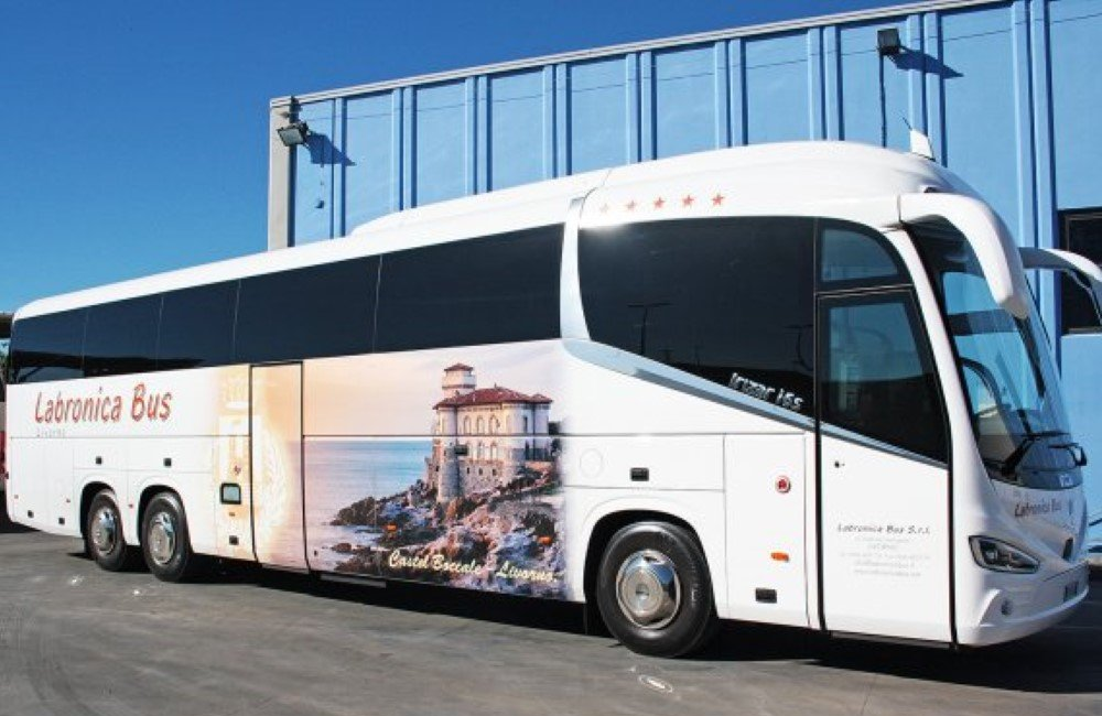 Un autobus Labronica bianco parcheggiato all'aperto con un grande adesivo raffigurante un edificio costiero in pietra sul fianco.