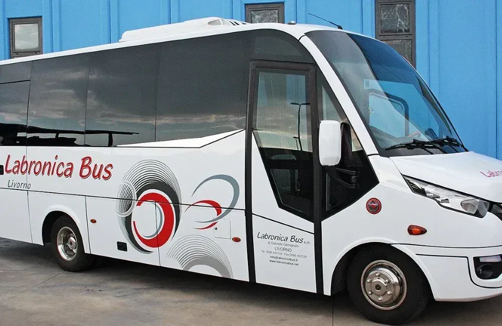 Un autobus Labronica bianco di medie dimensioni parcheggiato contro un edificio rivestito di pannelli blu.