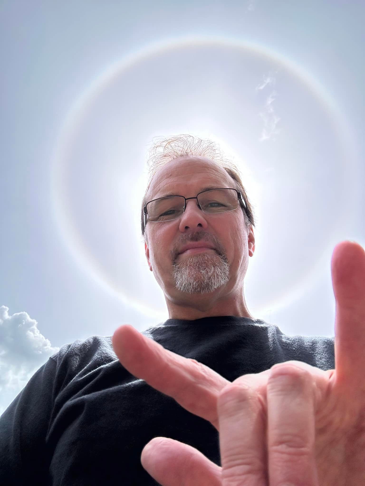 A man with glasses and a beard is making a peace sign