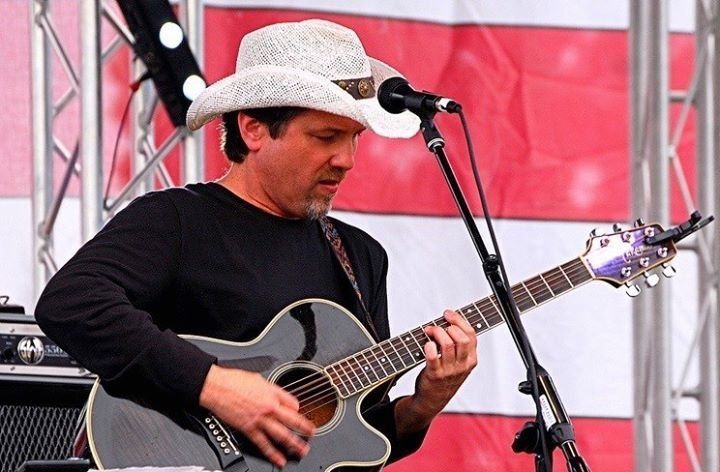 A man in a cowboy hat is playing a guitar and singing into a microphone
